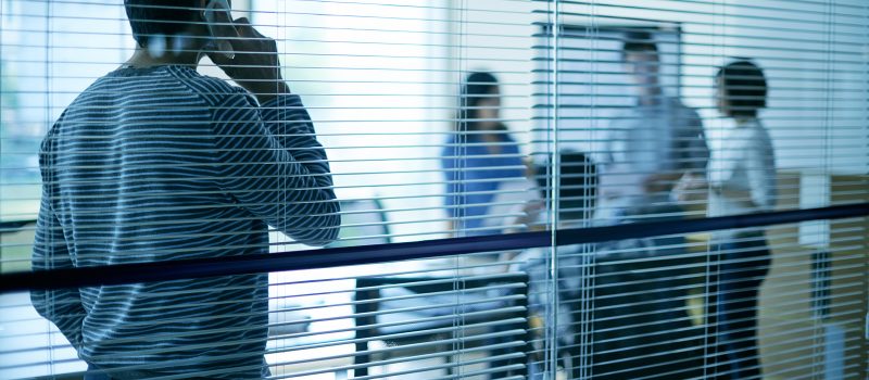Man talking on the phone in a conference room, obscured partially by blinds